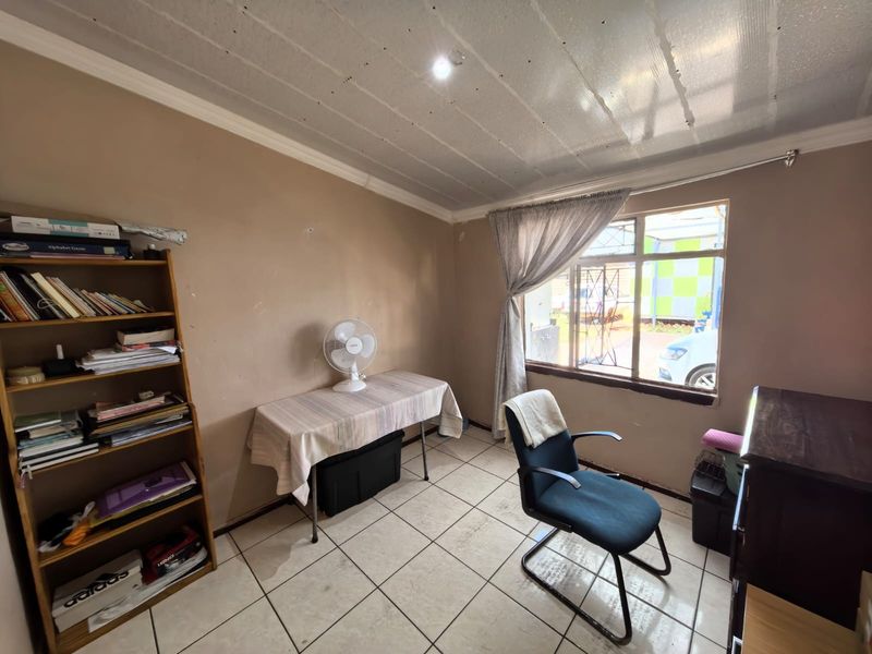A bedroom featuring tiled flooring, security bars on the window, and ceiling panels, currently used as a home office space.