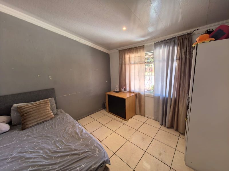 A bedroom featuring tiled flooring, security bars on the window, and crown molding. The space requires cosmetic updates to the walls and flooring.