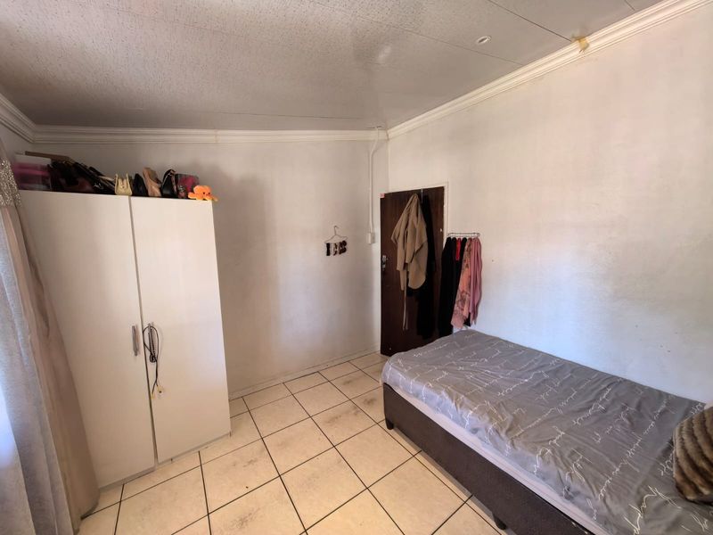 A compact bedroom featuring tiled flooring and standard ceiling finishes, requiring cosmetic updates to improve the overall aesthetic and condition.