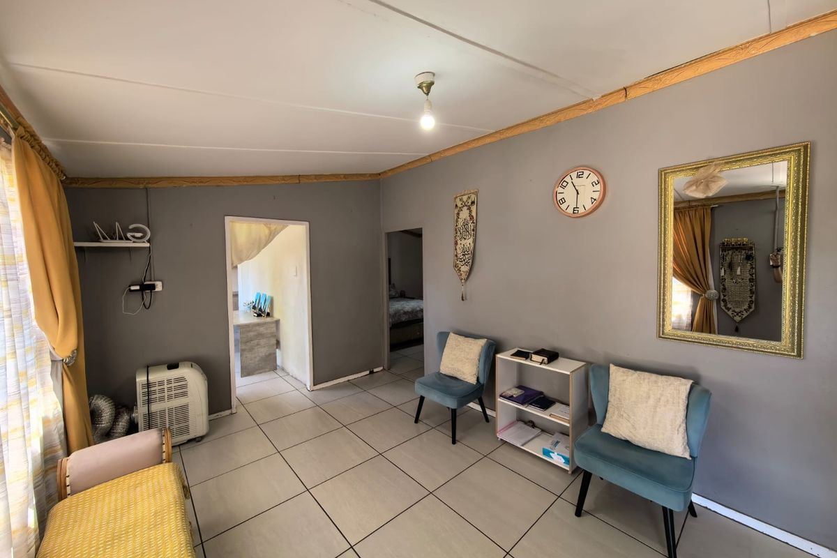 A living area featuring tiled flooring and neutral grey walls, providing a functional space with access to adjacent rooms.