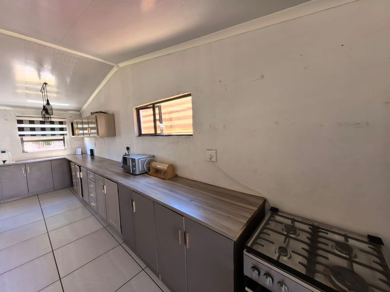 A functional kitchen featuring grey built-in cabinetry, wood-look laminate countertops, a gas stove, and tiled flooring under a sloped ceiling.
