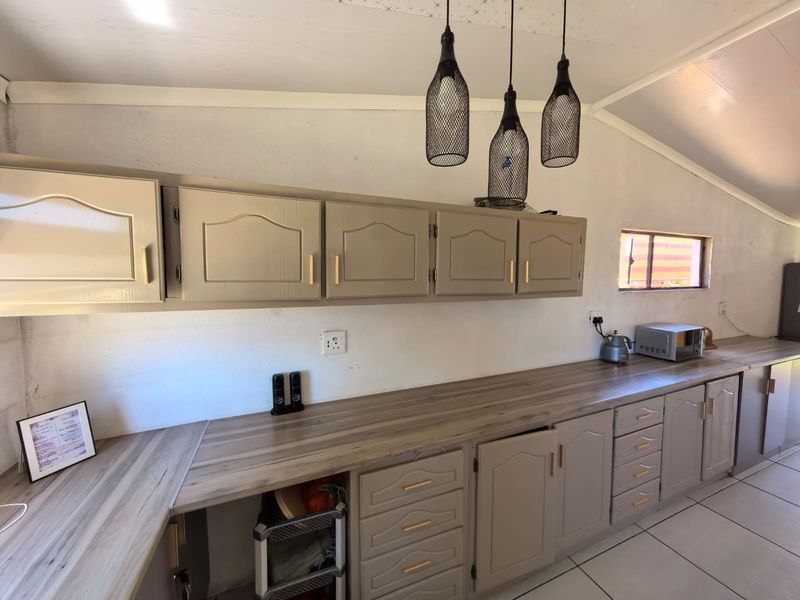 Kitchen area featuring neutral-toned built-in cabinetry, wood-look laminate countertops, and tiled flooring, illuminated by modern pendant lights.