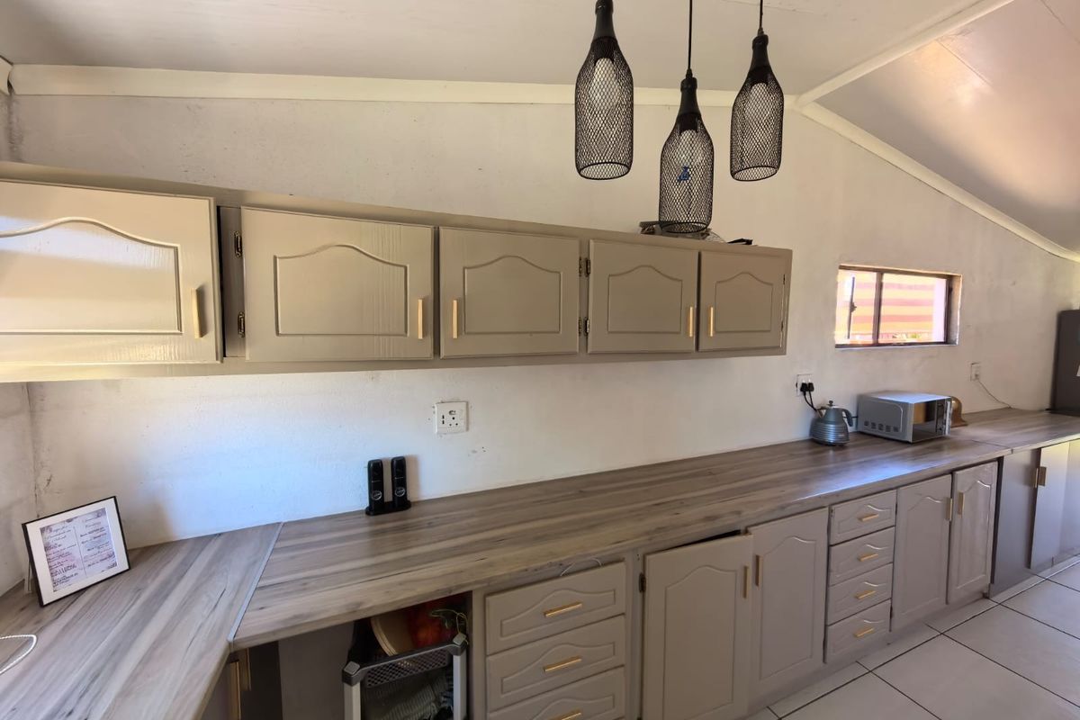 Kitchen area featuring neutral-toned built-in cabinetry, wood-look laminate countertops, and tiled flooring, illuminated by modern pendant lights.