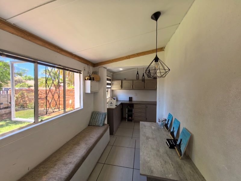 A functional kitchen area featuring built-in cabinetry, tiled flooring, and a built-in bench seat overlooking the garden through large windows.