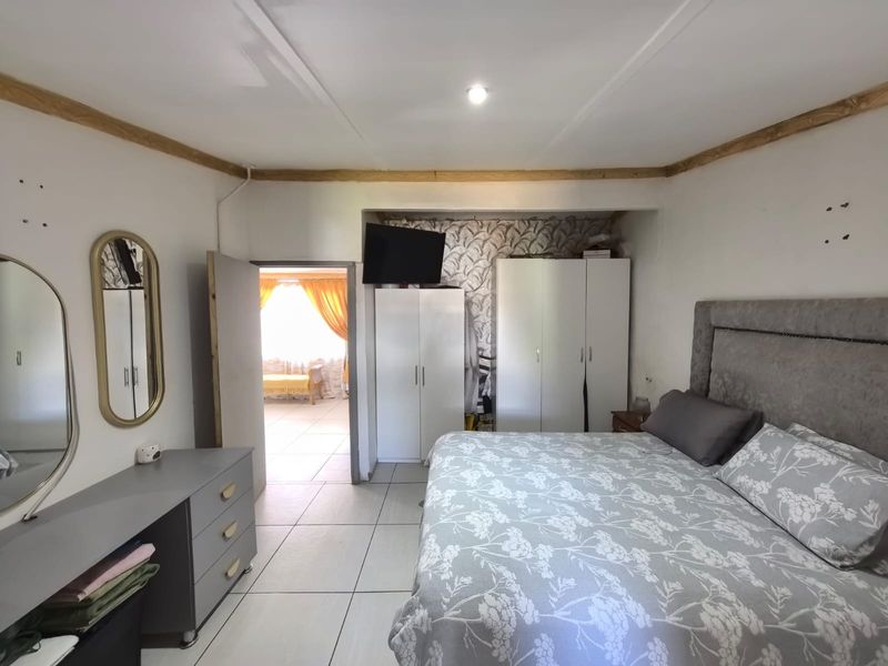 A bedroom featuring tiled flooring, built-in cupboards, and a wallpapered feature wall, with an adjacent room visible through the doorway.