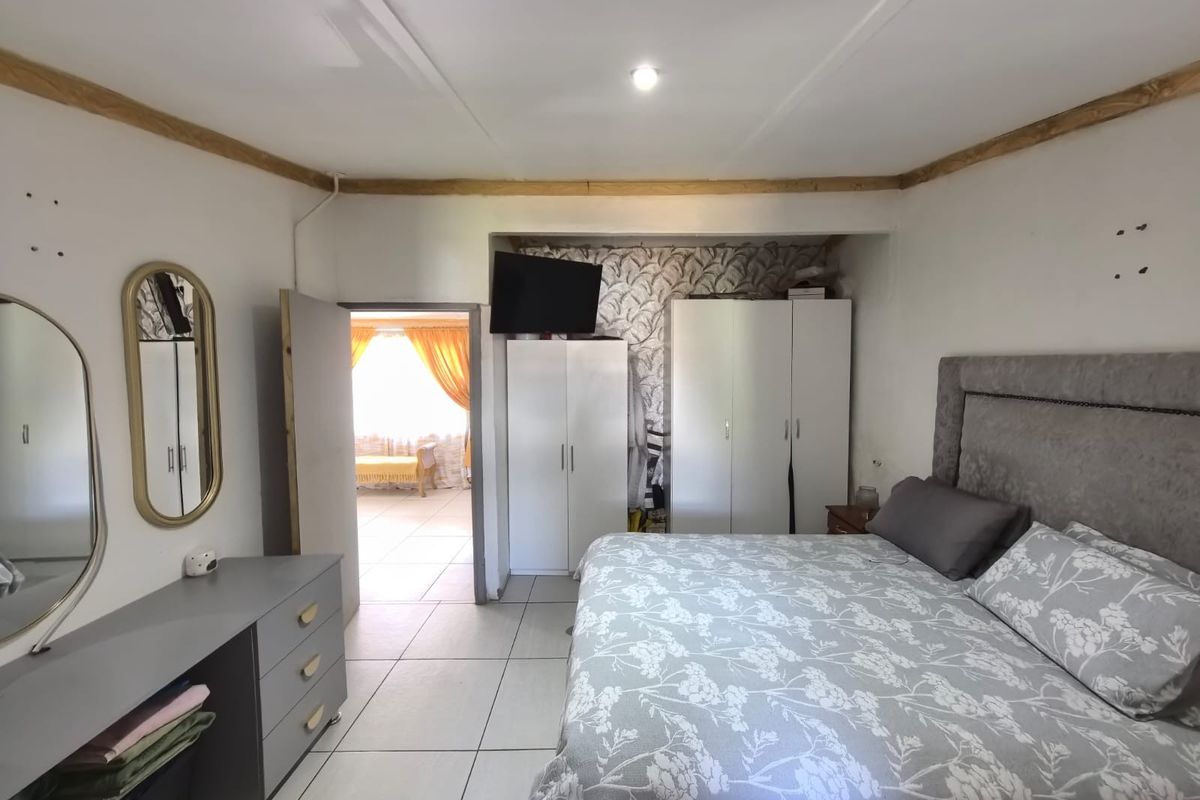 A bedroom featuring tiled flooring, built-in cupboards, and a wallpapered feature wall, with an adjacent room visible through the doorway.