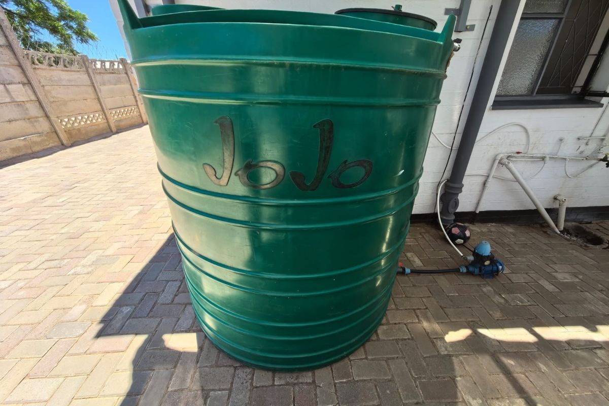 A green JoJo water storage tank with an integrated pump system located on a paved rear patio area.