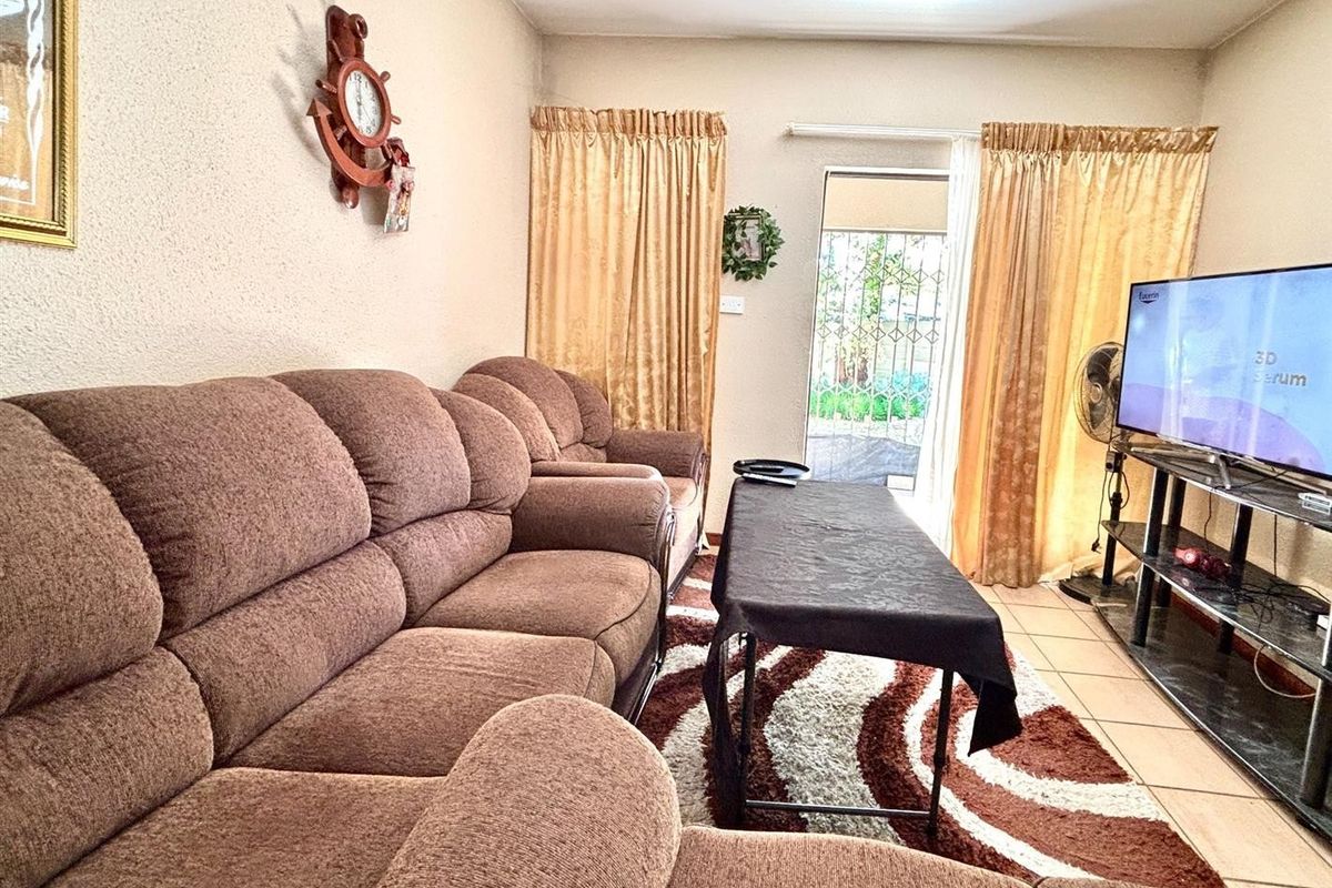 A living room featuring tiled flooring and a sliding door with an integrated security gate, providing access to the exterior.