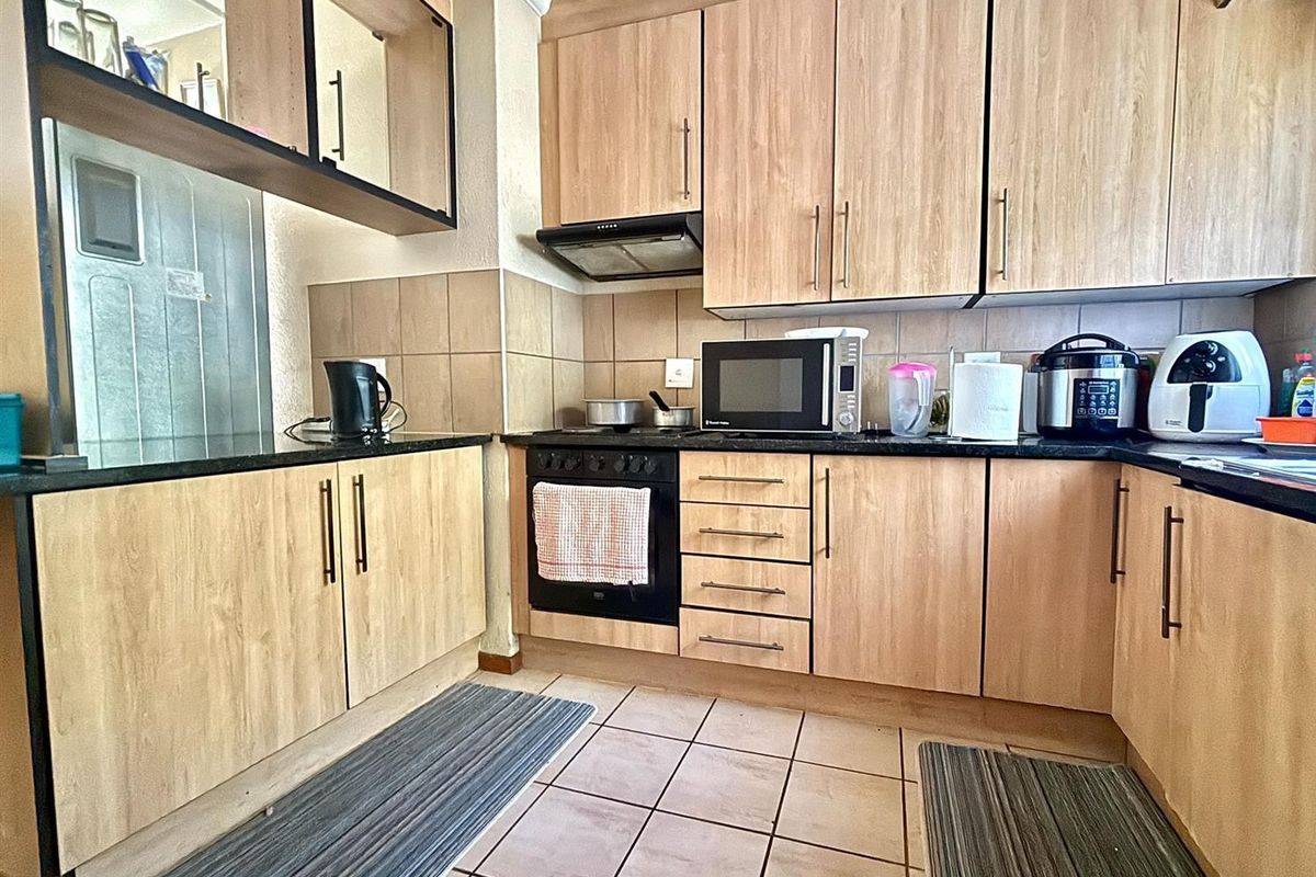 Functional kitchen featuring light wood-tone cabinetry, dark granite countertops, built-in oven with extractor fan, and tiled flooring.