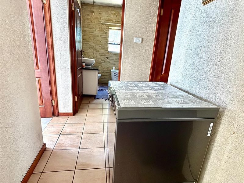 A functional hallway featuring tiled flooring and wooden door frames, providing access to adjacent rooms including a bathroom with stone-cladding detail.