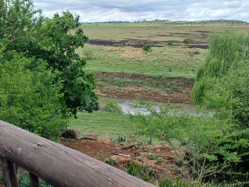 Scenic view overlooking a river and expansive green farm landscape from a wooden balcony railing.