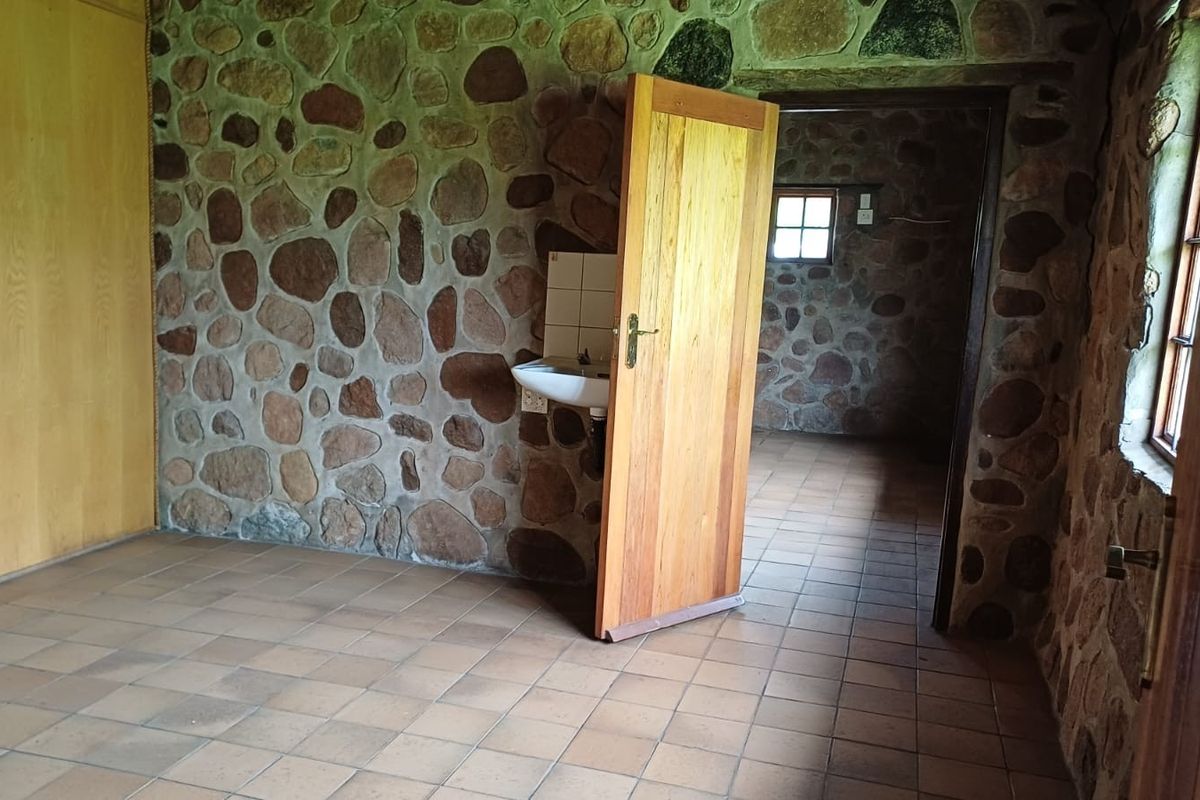 A rustic bedroom featuring exposed stone walls, tiled flooring, and a built-in cupboard, with an integrated wall-mounted basin and timber door access.