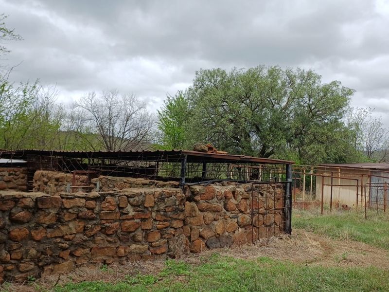 An outdoor farm area featuring weathered stone walls and rusted metal structures, indicating a need for significant maintenance or structural restoration.