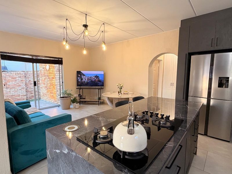 Modern open-plan living area featuring a sleek kitchen island with a built-in gas hob, dark cabinetry, and seamless access to the outdoor patio.