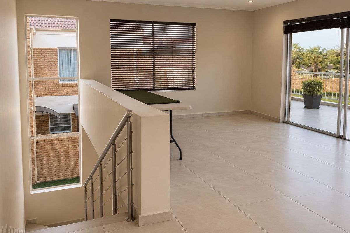 A bright, open-plan living area featuring neutral tiled flooring, a modern staircase with stainless steel balustrades, and large sliding doors leading to a balcony.