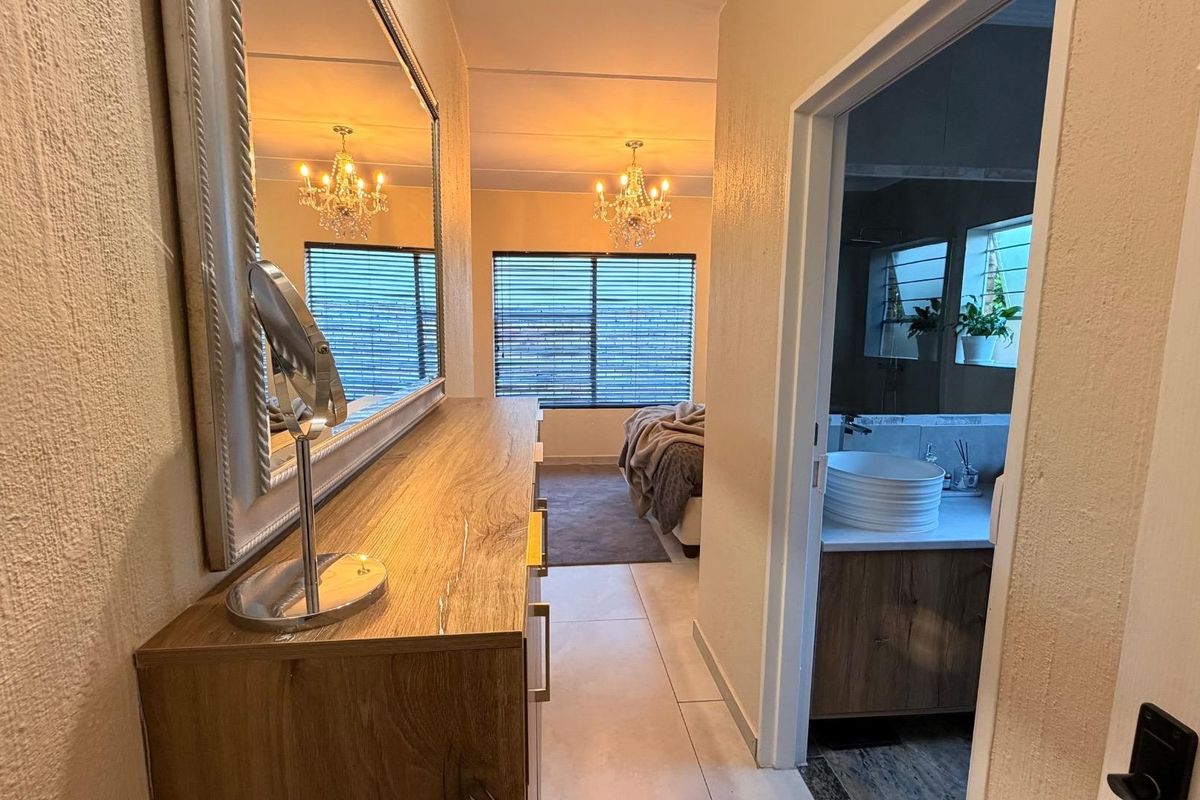 A well-lit bedroom featuring tiled flooring, venetian blinds, and an adjoining en-suite bathroom with modern vanity cabinetry.