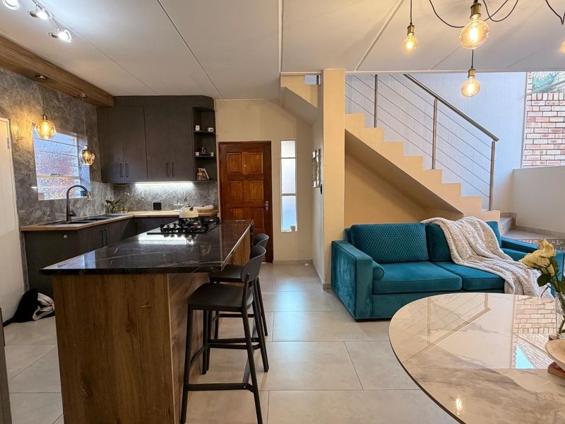 Modern open-plan living area featuring a contemporary kitchen with a central island, gas hob, and a staircase with a sleek metal railing.