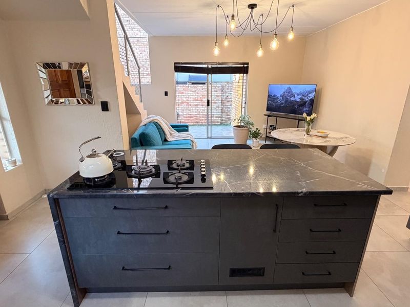 Modern open-plan living area featuring a central kitchen island with a gas hob, tiled flooring, and direct access to an outdoor patio.