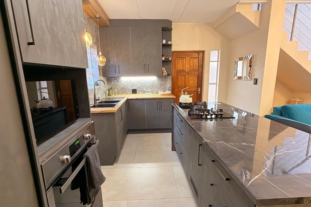 Modern kitchen featuring dark cabinetry, stone countertops, a central island with a gas hob, and integrated oven, complemented by tiled flooring.
