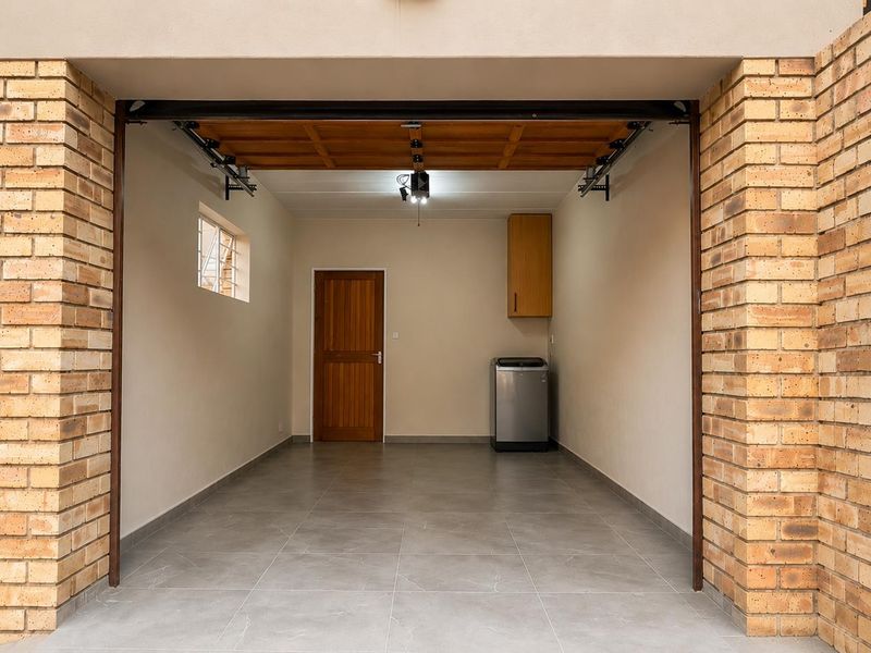 A clean, well-maintained garage featuring tiled flooring, a timber door, and a built-in wall cabinet, providing secure parking and additional storage space.