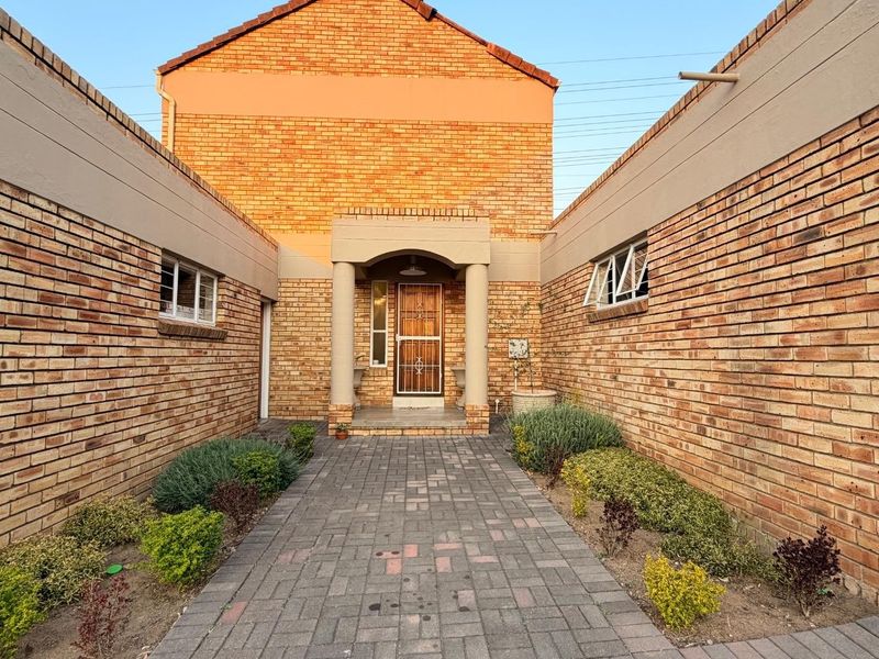 Front entrance of a brick-faced house featuring a paved walkway leading to a covered porch with a security gate.