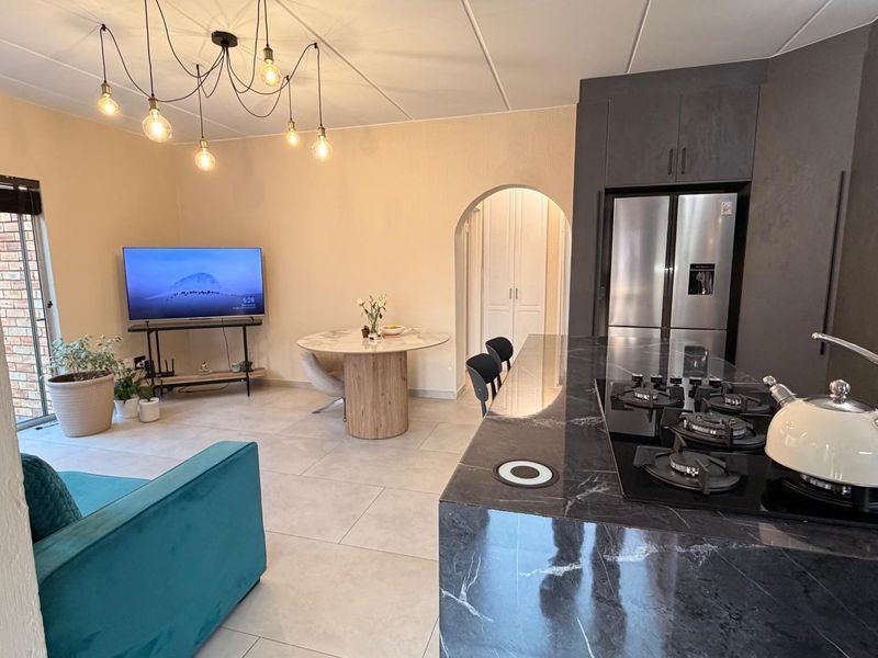 Modern open-plan living area featuring a sleek kitchen with a marble-look island, gas hob, built-in oven, and tiled flooring throughout.