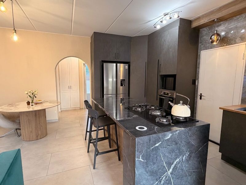Modern open-plan kitchen featuring a large stone-topped island with integrated gas hob, sleek cabinetry, and contemporary pendant lighting, seamlessly flowing into the dining area.