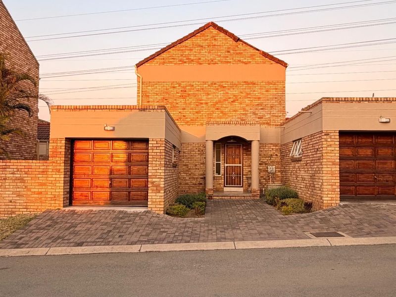 Front elevation of a brick house featuring a double garage, paved driveway, and a covered entrance with a security gate.