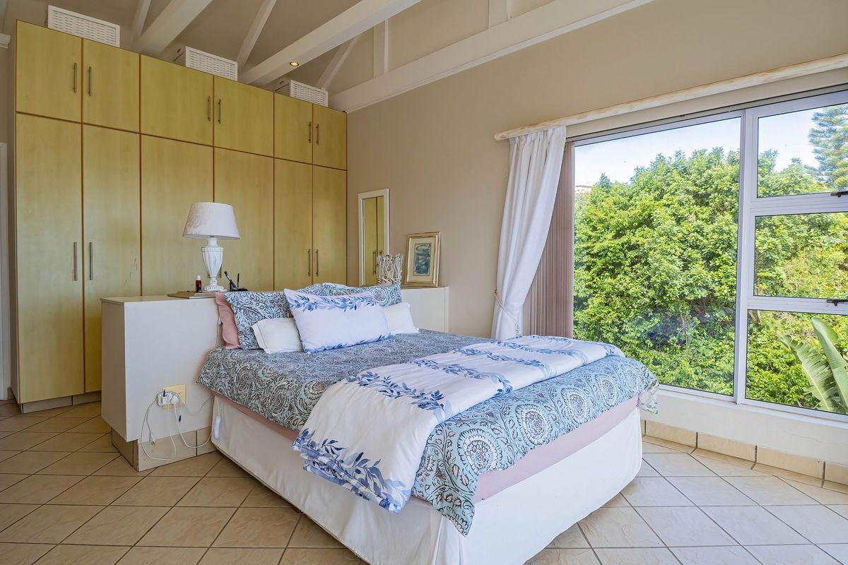 Spacious bedroom featuring built-in cupboards, exposed rafters, and large windows providing natural light and garden views.