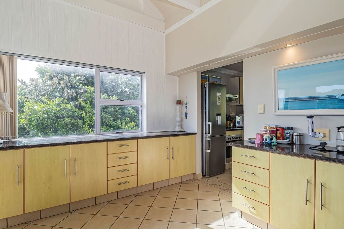 A functional kitchen featuring light wood cabinetry, dark granite countertops, tiled flooring, and a large window providing natural light and garden views.