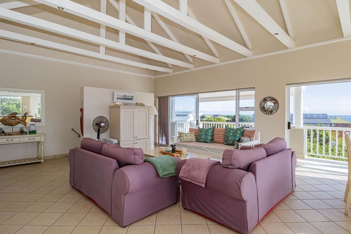 Spacious living room featuring high vaulted ceilings with exposed white beams, tiled flooring, and large sliding doors opening to a balcony with ocean views.