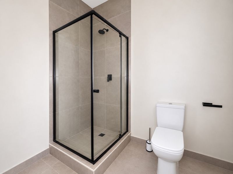 Modern bathroom featuring a corner shower enclosure with black frame, neutral wall and floor tiling, and a white toilet.