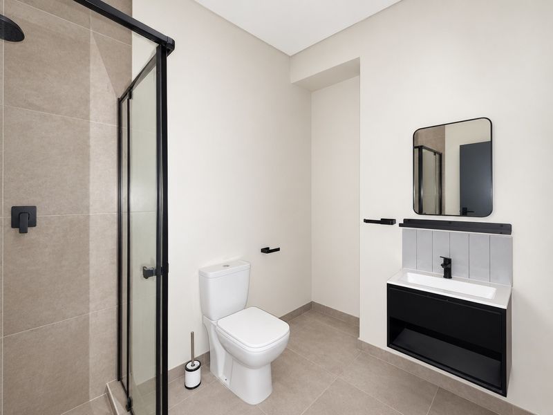 Modern bathroom featuring a walk-in shower with black frame, wall-mounted vanity with integrated basin, and contemporary black fixtures.