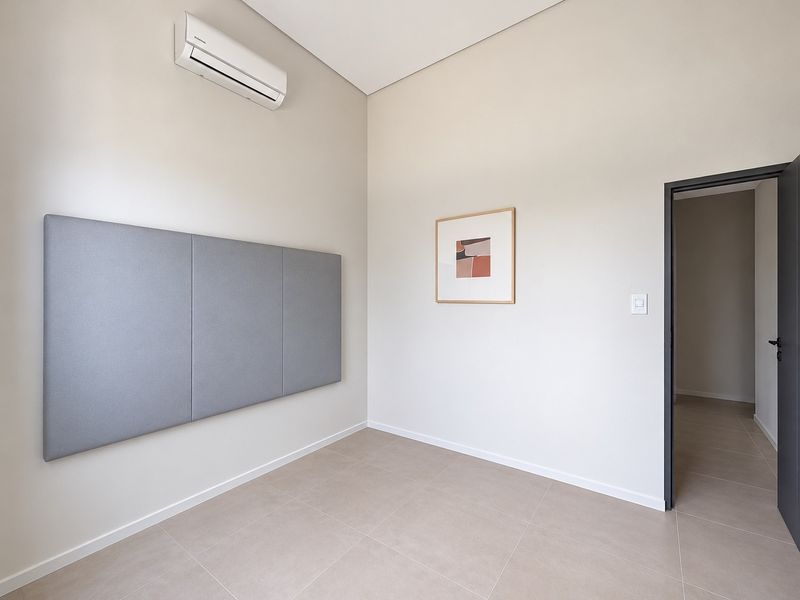 A clean, modern bedroom featuring neutral tiled flooring, a wall-mounted split-system air conditioner, and acoustic wall paneling.