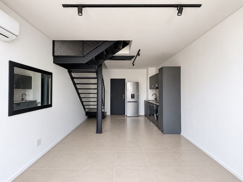 Modern open-plan living area featuring a sleek kitchen with built-in appliances, tiled flooring, and a striking industrial-style metal staircase.