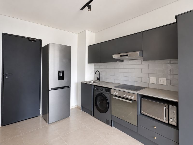 Modern kitchen featuring sleek dark grey cabinetry, subway tile backsplash, integrated oven, hob, extractor fan, and tiled flooring.
