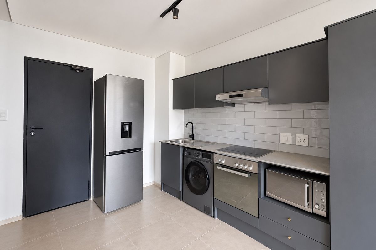 Modern kitchen featuring sleek dark grey cabinetry, subway tile backsplash, integrated oven, hob, extractor fan, and tiled flooring.