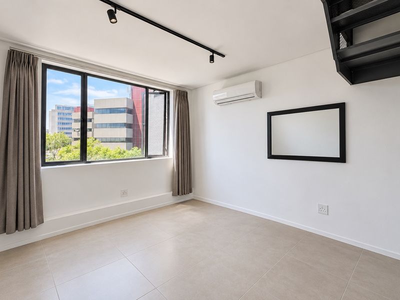 A bright, modern living area featuring tiled floors, track lighting, a split-system air conditioner, and large windows with urban views.