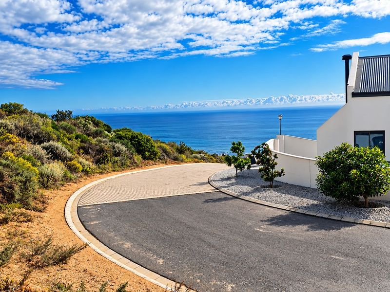 A well-maintained front entrance featuring a paved and asphalt driveway, landscaped garden, and a clear view of the ocean.