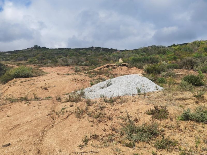 A view of a vacant residential plot featuring natural terrain and a paved verge, ready for development.
