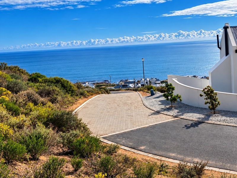 A scenic view overlooking the coastline and ocean, featuring a paved driveway and modern retaining wall structure.