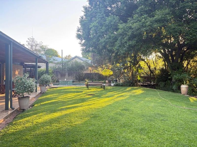 Spacious private garden featuring a well-maintained lawn, mature trees, a covered patio area, and a swimming pool.