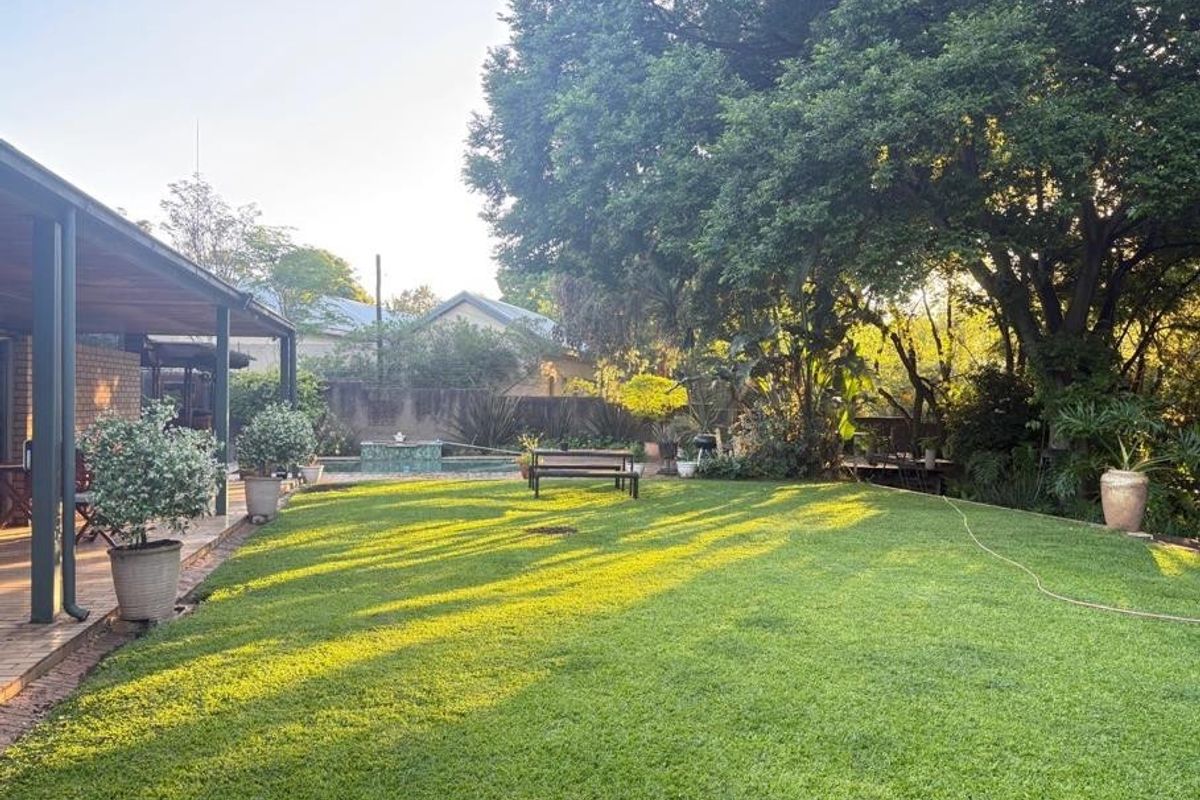 Spacious private garden featuring a well-maintained lawn, mature trees, a covered patio area, and a swimming pool.