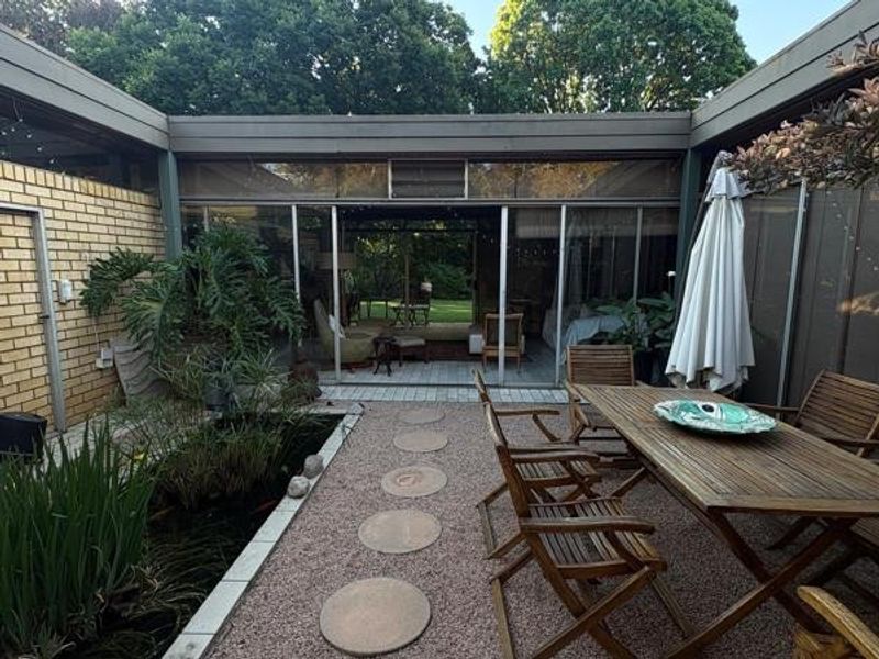 A private courtyard patio featuring a built-in pond, paved walkway, and large sliding glass doors providing seamless access to the interior living space.