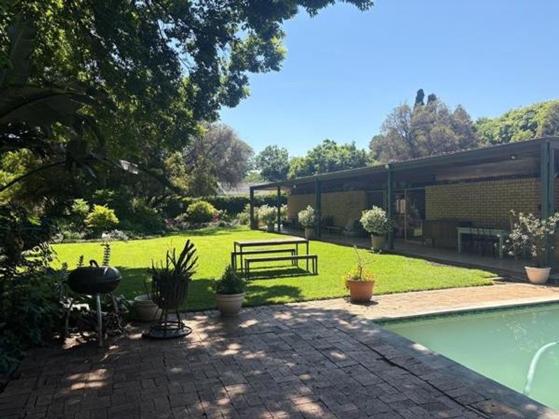 Spacious outdoor area featuring a swimming pool, brick-paved patio, and a covered veranda overlooking a well-maintained garden and lawn.