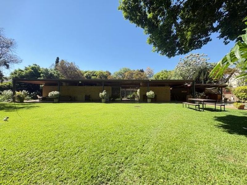 Spacious rear garden featuring a large manicured lawn and a covered patio area, providing an ideal space for outdoor relaxation and entertainment.