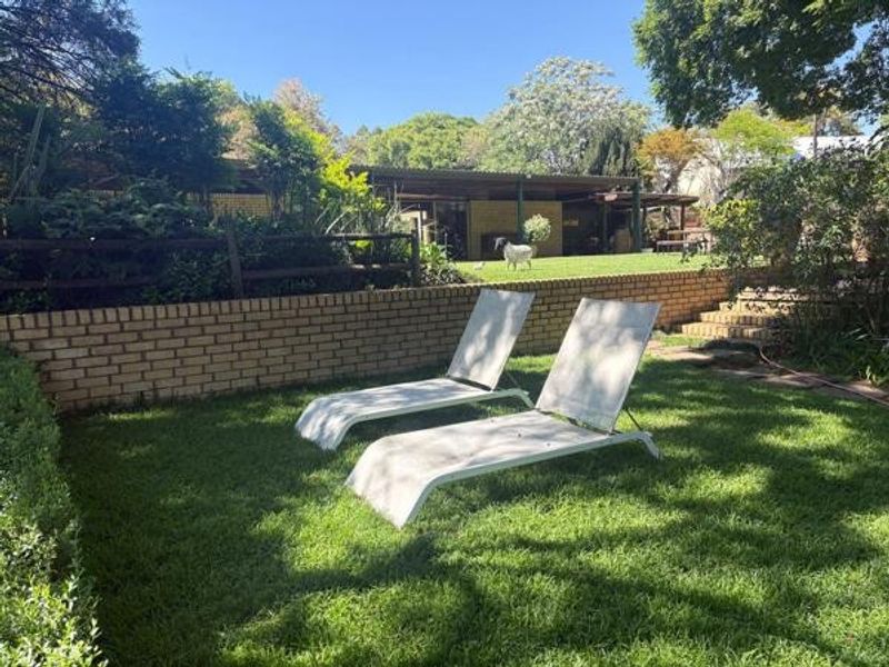 A spacious garden area featuring a brick retaining wall, tiered brick stairs, and a covered patio overlooking the lawn.