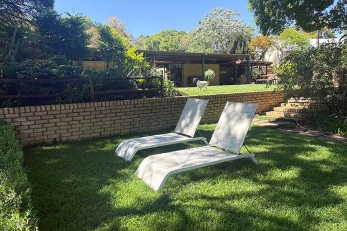 A spacious garden area featuring a brick retaining wall, tiered brick stairs, and a covered patio overlooking the lawn.