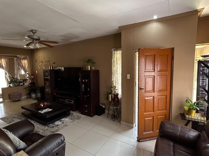Spacious living room featuring tiled flooring, a ceiling fan, and recessed lighting, with direct access to an adjacent area through a panelled door.