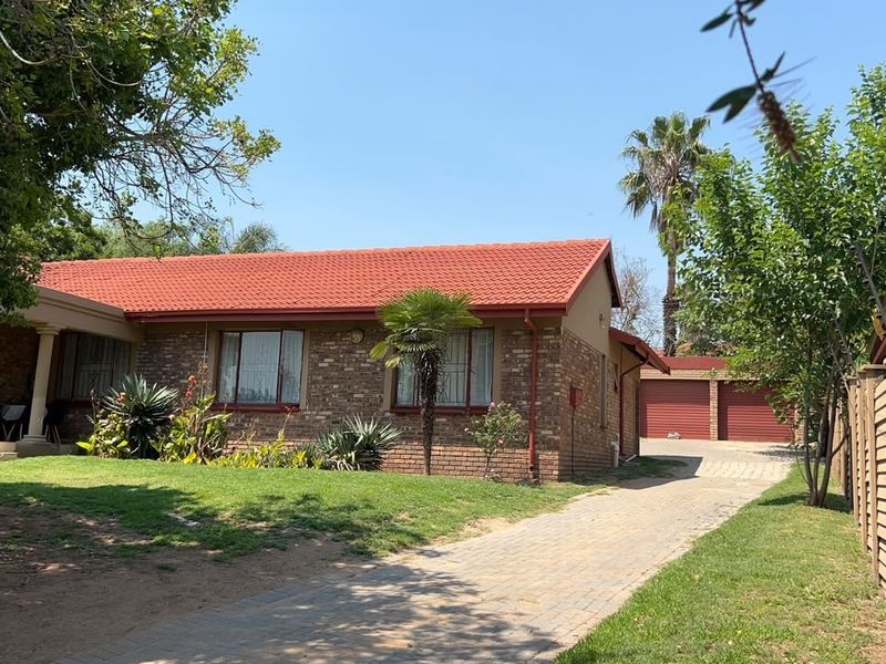 A single-story brick house featuring a tiled roof, a paved driveway leading to a double garage, and a covered front porch.